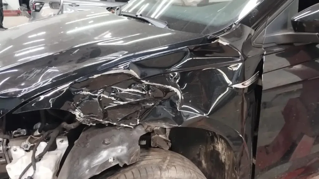 Detalhe do capô e para-lama dianteiro esquerdo do VW Virtus Highline 2025 deformados por colisão frontal — antes da troca de peças na Lisboa Car Service Porto Alegre